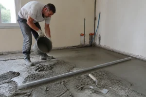 Artisan préparant et étalant une chape maigre au sol avec une truelle sur un chantier de rénovation