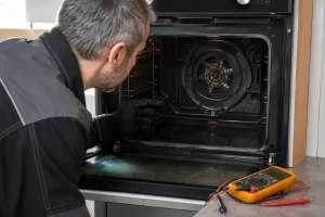 Technicien inspectant la résistance circulaire d'un four électrique débranché avec un multimètre à proximité